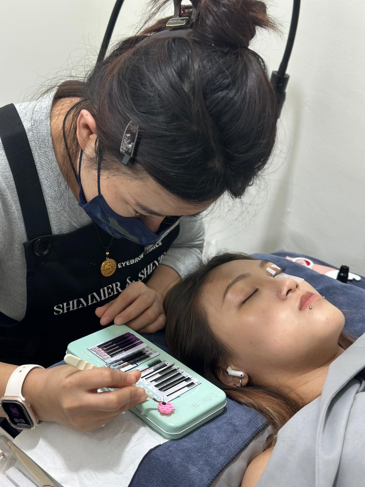 Person getting eyelash extensions from another person in a salon setting.